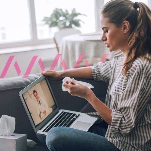 Image of woman, sitting with a laptop. She’s holding a tissue and conducting a virtual doctor’s visit.