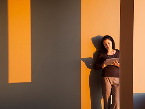 Female executive using a notebook computer and leaning up against an office wall in late afternoon sun.