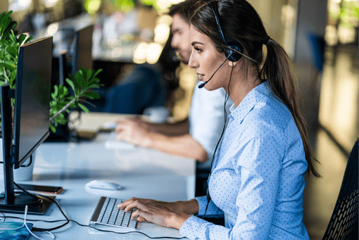 Photo of woman working in a call center. She is typing on her computer keyboard while talking to a customer over her headset.