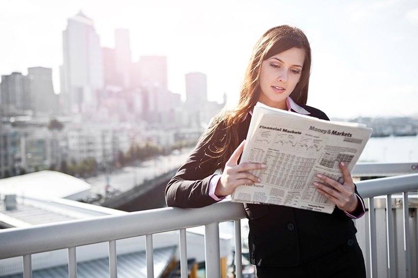 Woman leaning on fence reading newspaper